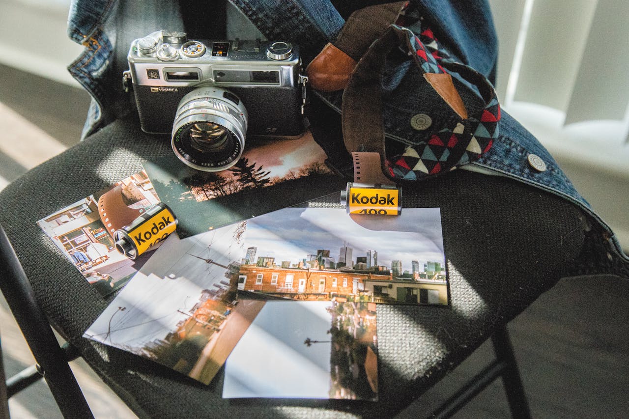 A vintage camera and Kodak film rolls placed on a dark chair with photographs.